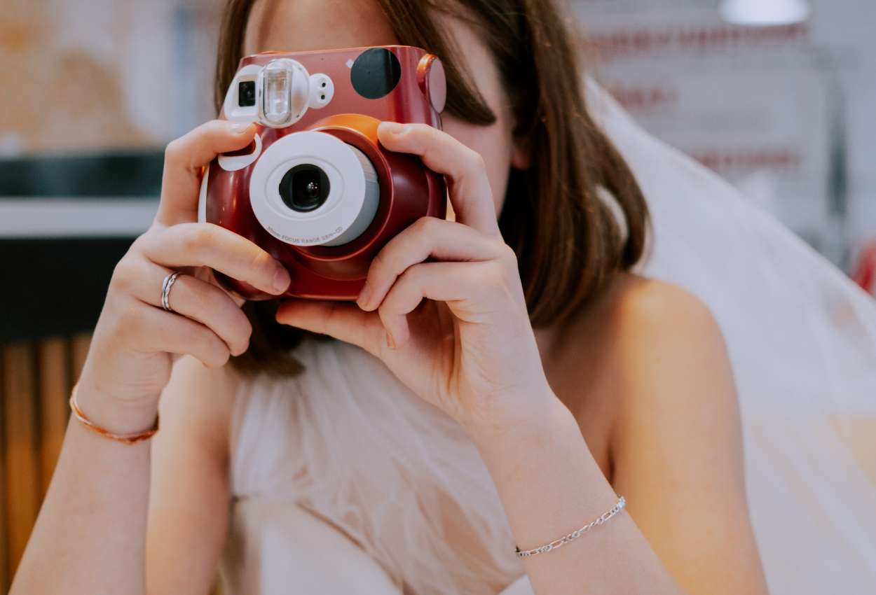 Une femme en robe blanche tient un appareil photo instantané rouge, capturant des idées photos baby shower.