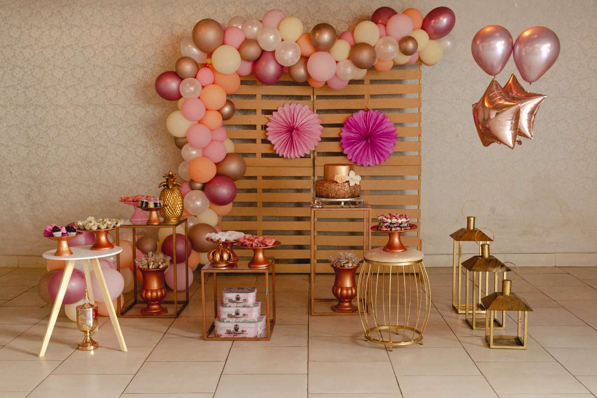 Décoration de baby shower avec ballons multicolores, gâteau sur table dorée et lanternes dorées, thème baby shower élégant et festif.